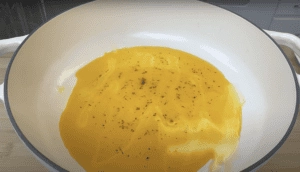Yellow liquid with herbs in a white bowl on a wooden surface, perfect for cooking recipes and food preparation.